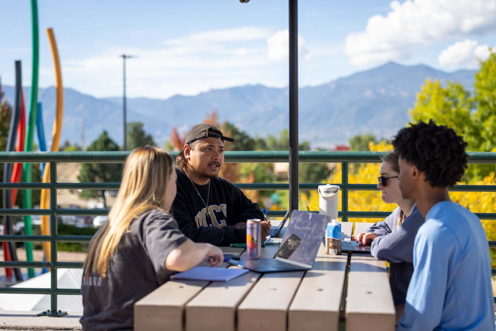 a group of students sitting outside the UC working on a project together